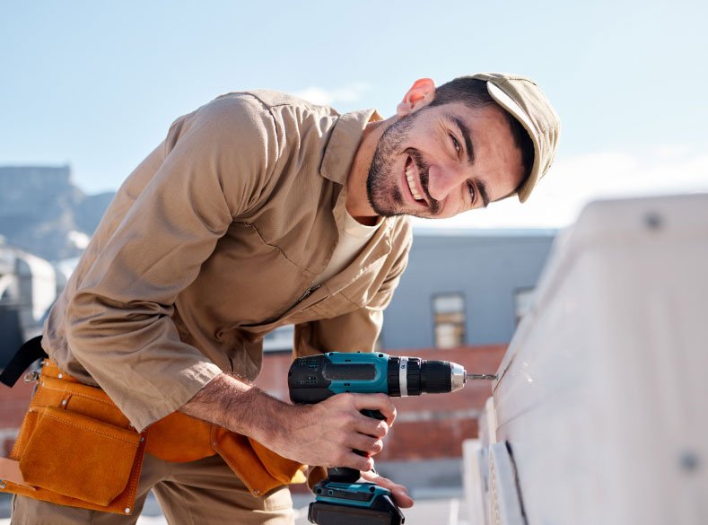 Smiling roofer holding a cordless drill before a roof replacement